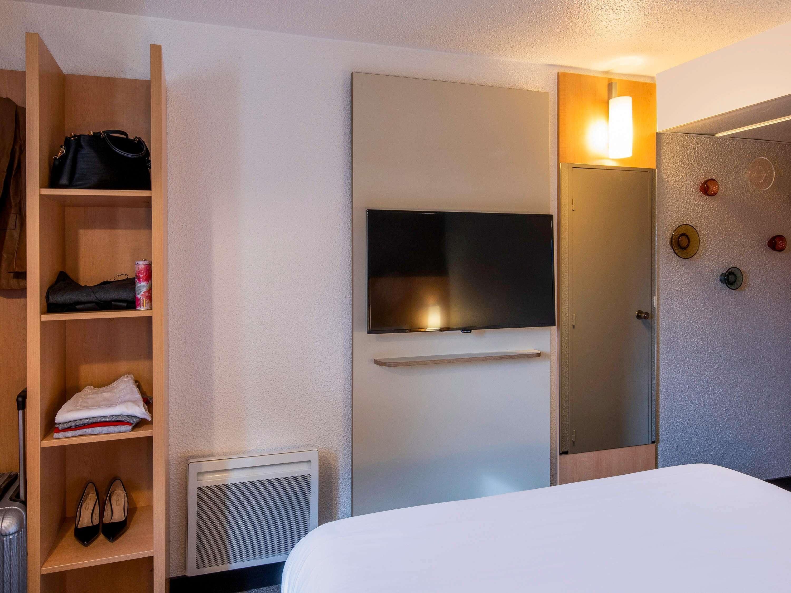 Une chambre d’hôtel équipée d’un lit, d’un téléviseur fixé au mur, d’une armoire et d’un porte-chaussures.
