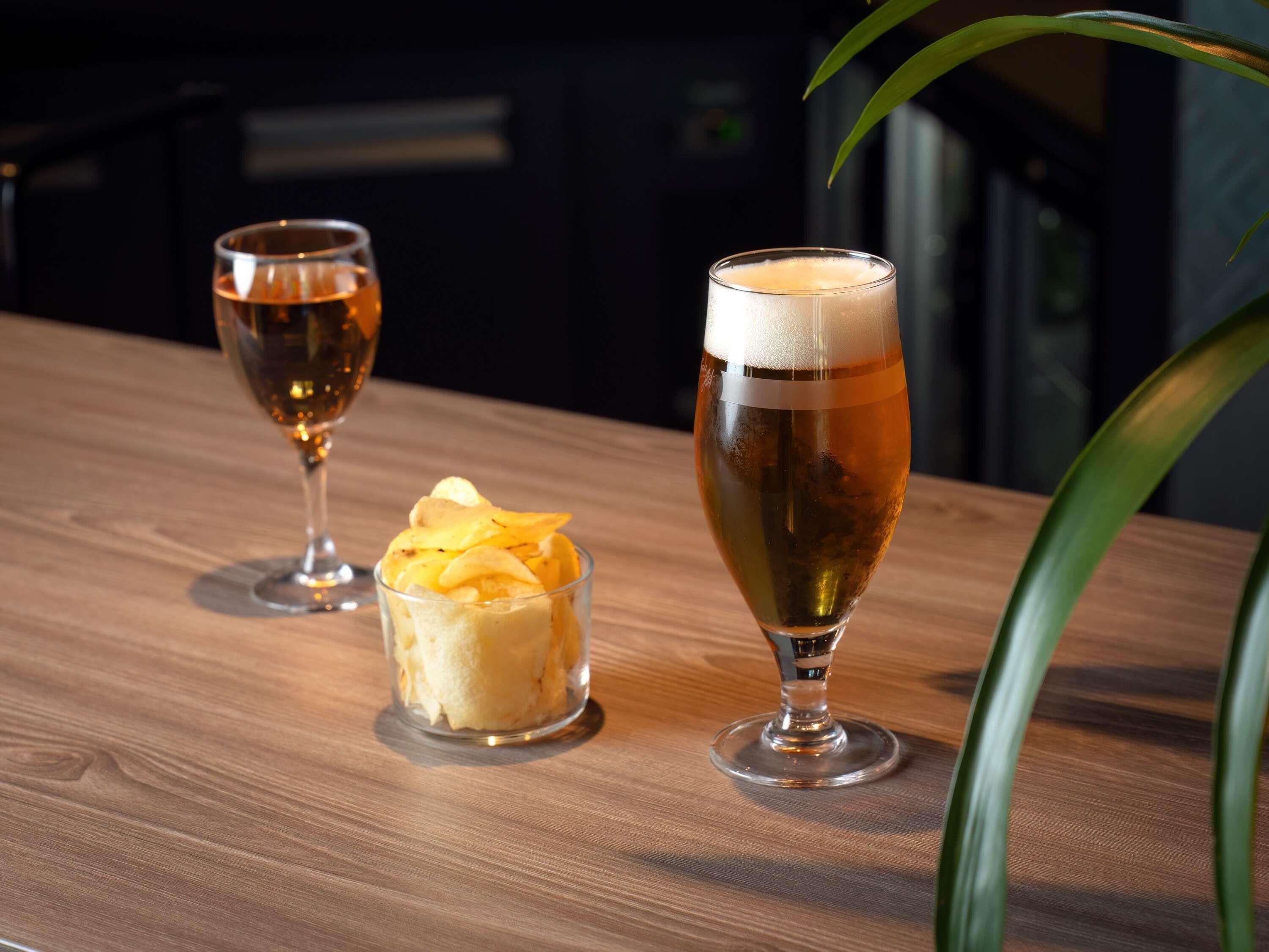Deux verres de bière sur une table en bois, avec une plante en arrière-plan.