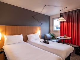 Habitación de hotel con dos camas, un escritorio, una computadora portátil, una cámara y una cortina roja.