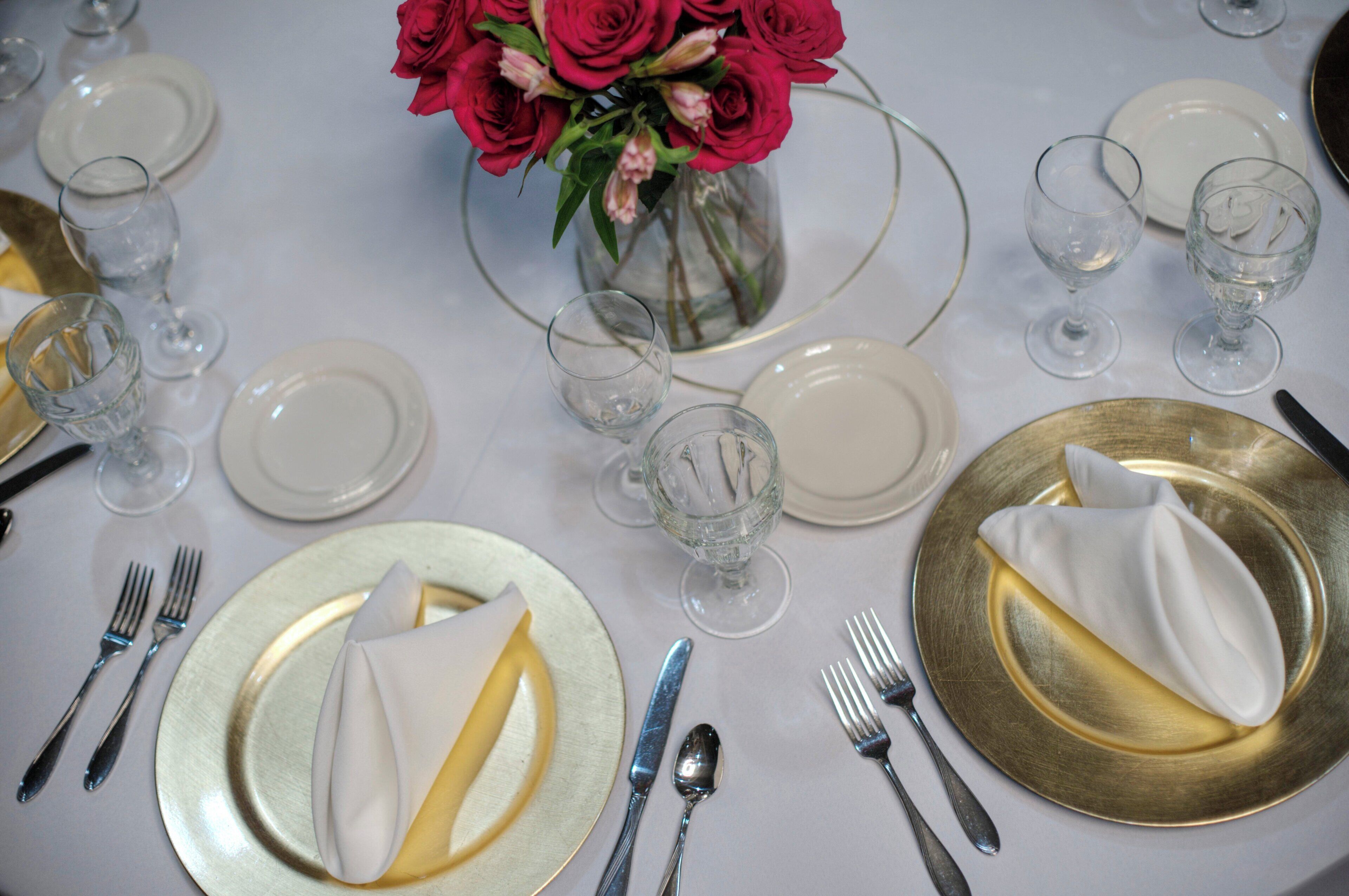 A table set for a formal meal with plates, cutlery, and a vase of flowers.