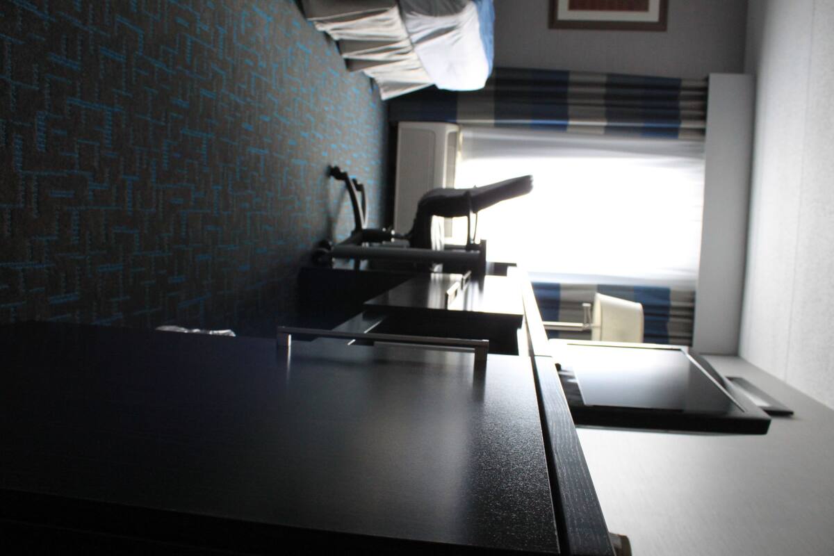 A room with a bed, a desk, and a window with blinds.