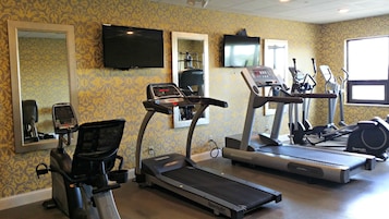 Un gimnasio con cintas de correr, bicicletas estáticas y un espejo grande.