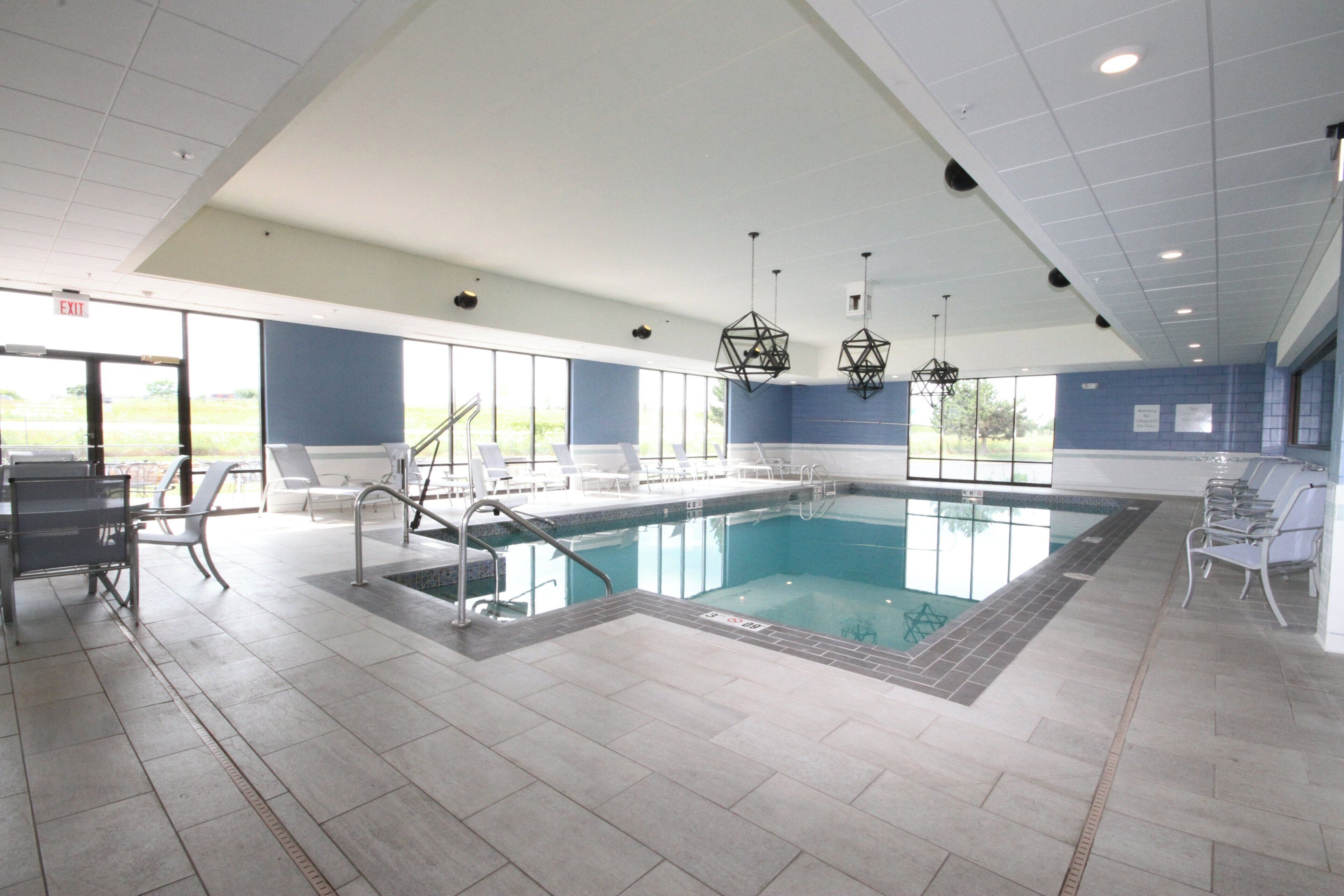 A swimming pool with a tiled deck, lounge chairs, and a view of the outdoors.