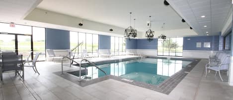 A swimming pool with a tiled deck, lounge chairs, and a view of the outdoors.