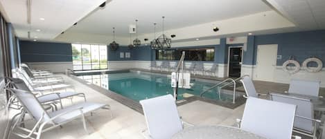 Zona de piscina con sillones de descanso y una mesa, un bar junto a la piscina y vistas al exterior.