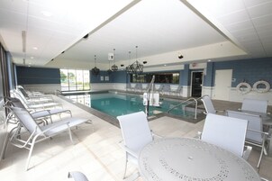 Zona de piscina con sillones de descanso y una mesa, un bar junto a la piscina y vistas al exterior.