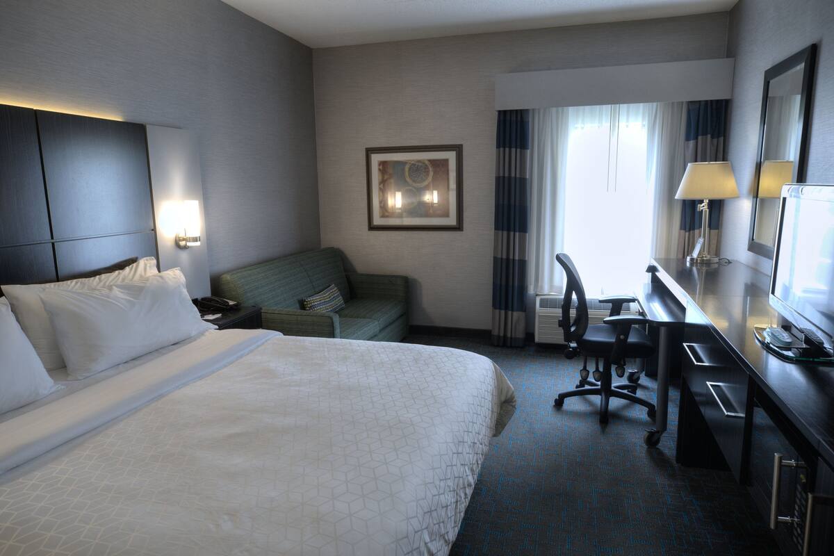 A hotel room with a large bed, a desk with a computer, a chair, and a couch.