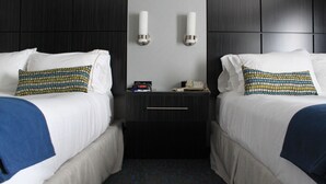 A hotel room with two beds, each with a patterned pillow, a bedside table with a clock and a phone, and a wall-mounted light fixture. - Holiday Inn Express Janesville - I-90 & US Hwy 14 by IHG (Janesville)