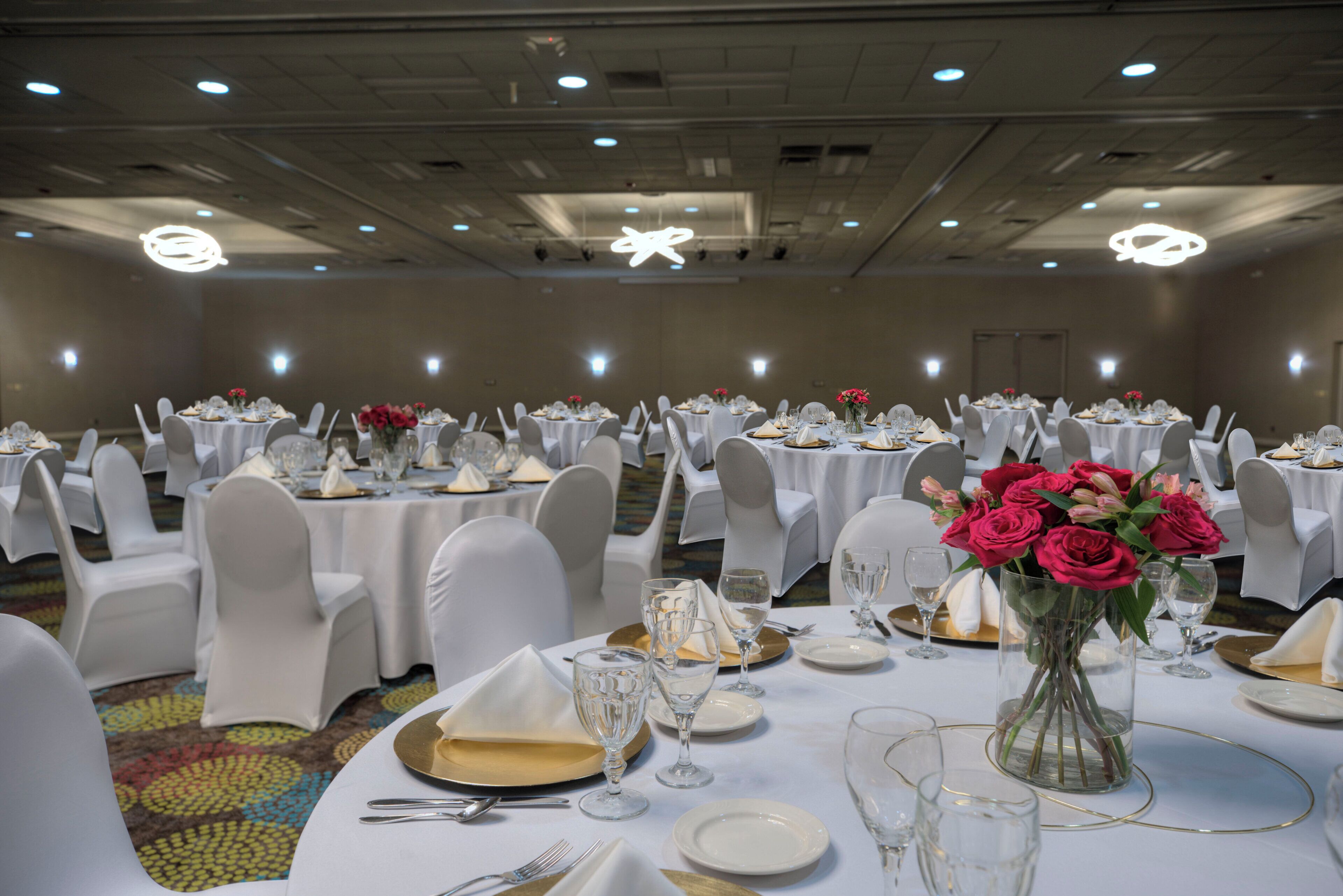 Een balzaal met ronde tafels gedekt voor een diner, witte stoelen en bloemrijke decoraties.