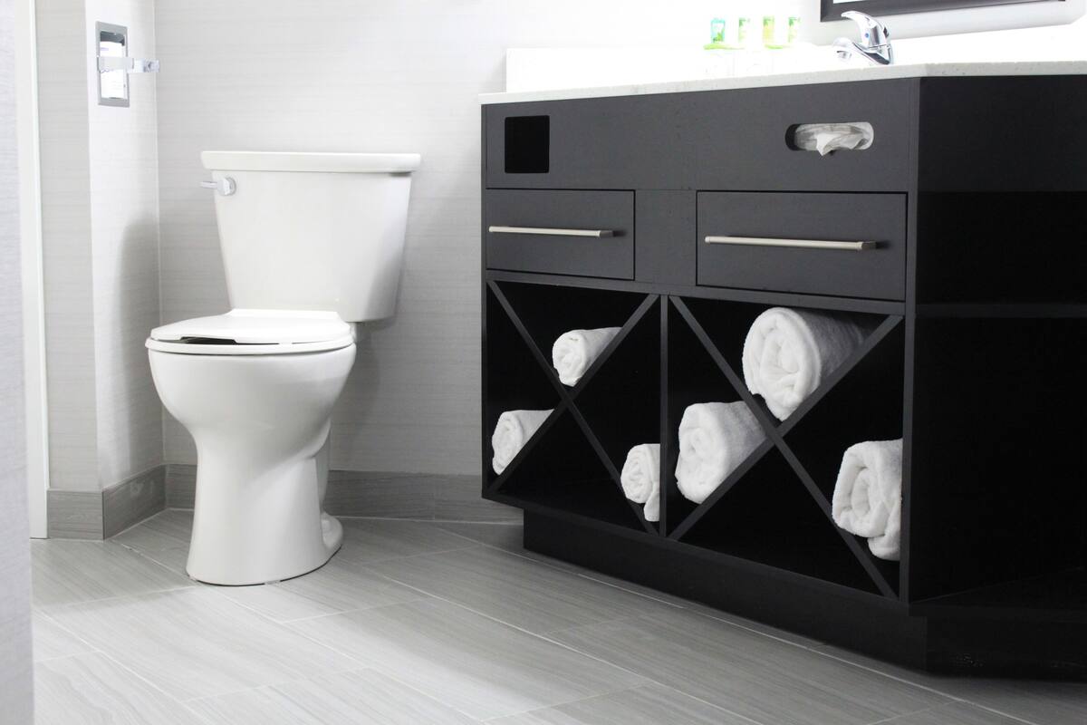 A modern bathroom with a white toilet, a black vanity with multiple towel compartments, and a white sink.