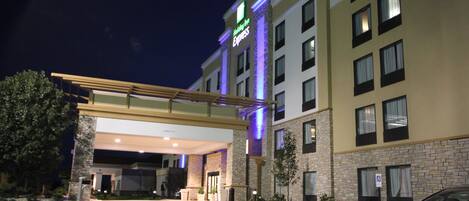 A hotel entrance with a covered walkway, a parking lot, and a building with multiple windows.