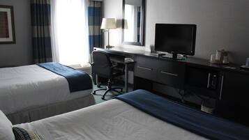 A hotel room with two beds, a desk with a computer, a chair, and a television.