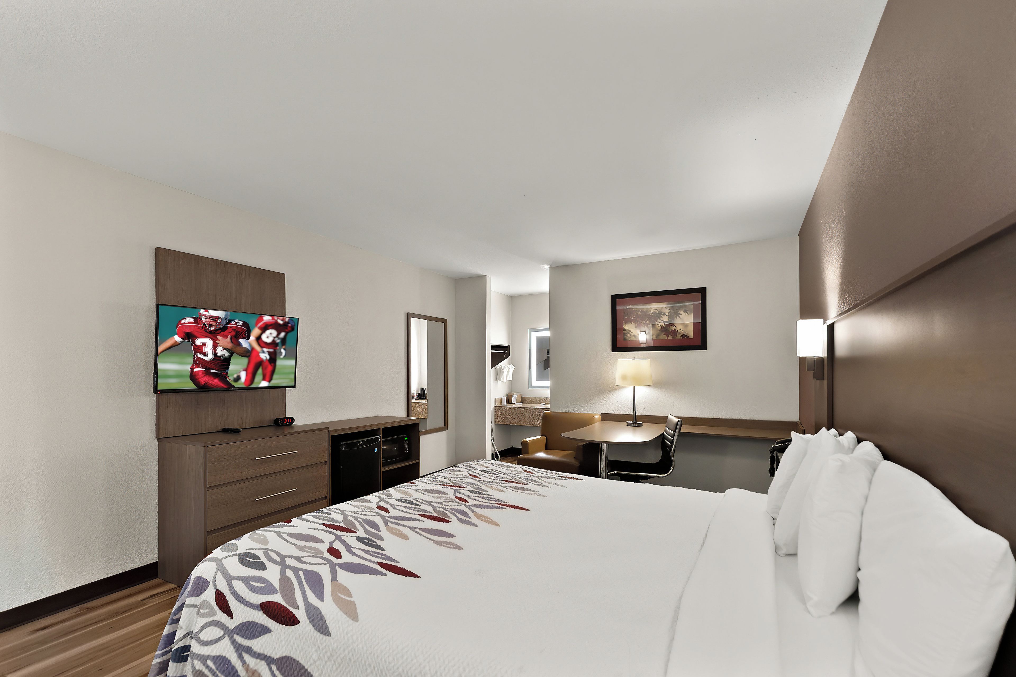 Une chambre d’hôtel équipée d’un lit, d’un bureau, d’une télévision, d ’un miroir et d’une lampe.