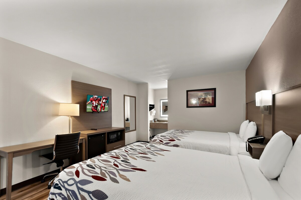 A hotel room with two beds, a desk, a TV, and a mirror.