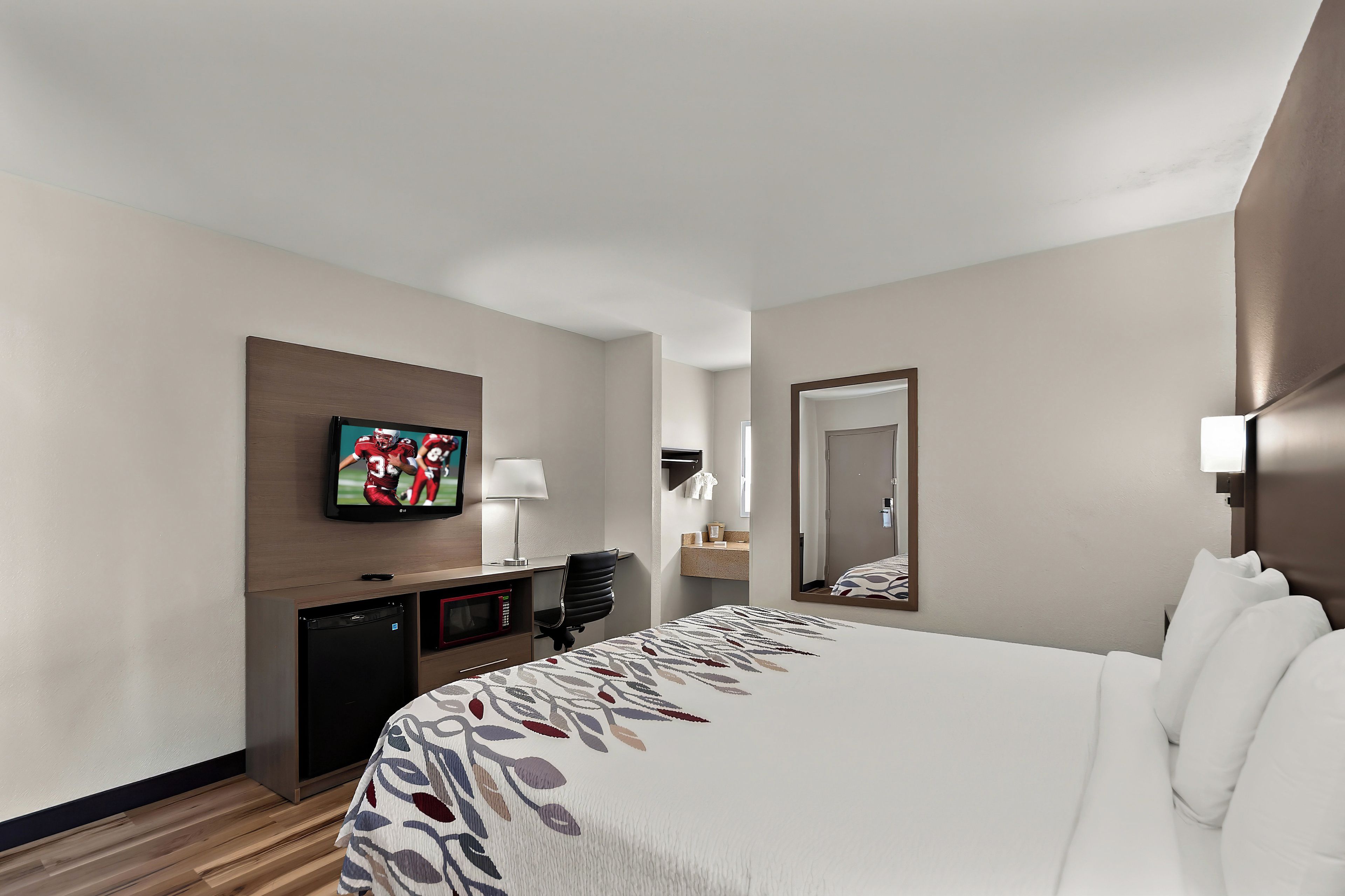 Una camera d'albergo con un letto, una televisione a parete, una scrivania con una lampada e uno specchio.