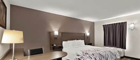 Habitación de hotel con cama, mesita de noche, lámpara, sillón y escritorio con silla.