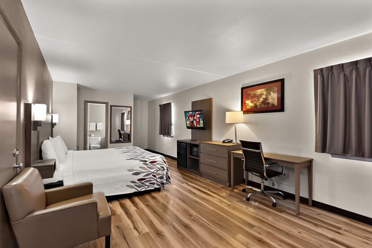 A hotel room with a bed, a desk, a chair, a TV, and a painting on the wall.