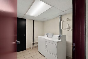 A laundry room with a front-loading washer and dryer, a black door, and a white tiled floor. - Red Roof Inn Winchester, VA (Winchester)