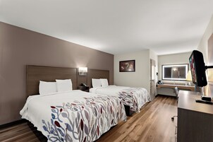 Habitación de hotel con dos camas, un escritorio, un televisor y una ventana.