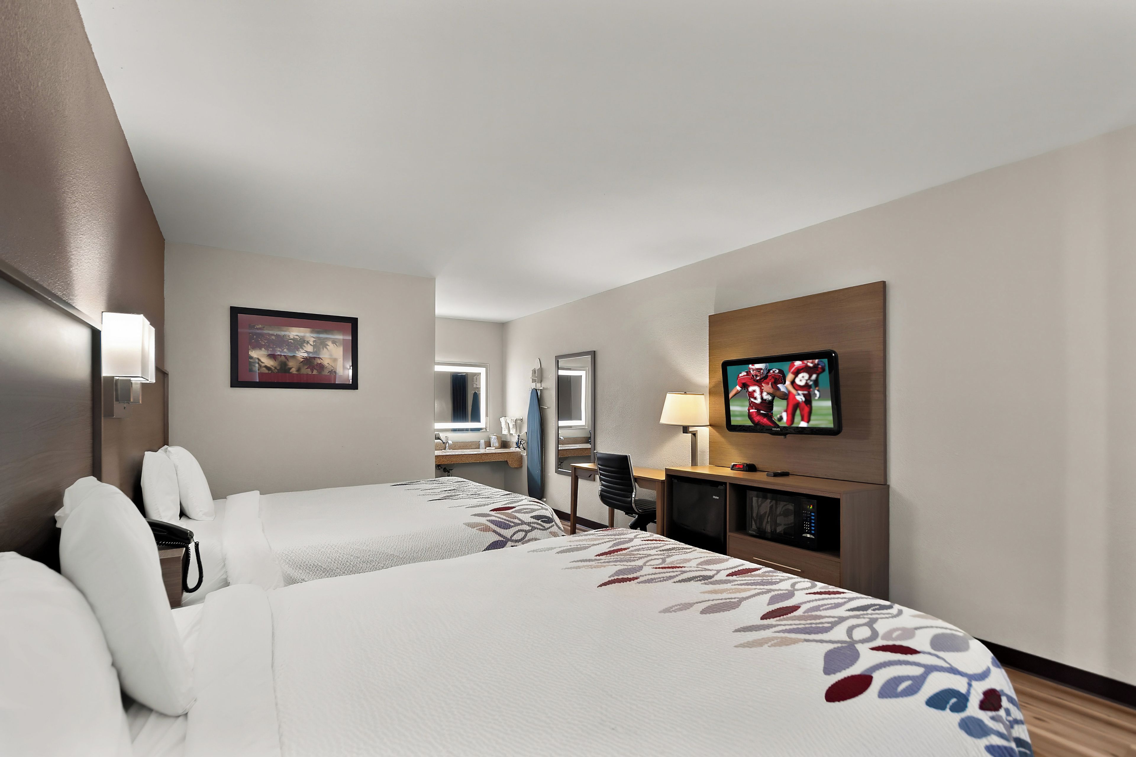 A hotel room with two beds, a TV, a desk, and a bathroom visible in the background.