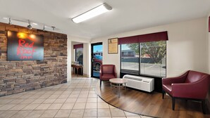 A Red Roof Inn lobby with a stone wall, a reception desk, a seating area with chairs, and a large window with blinds. - Red Roof Inn Winchester, VA (Winchester)