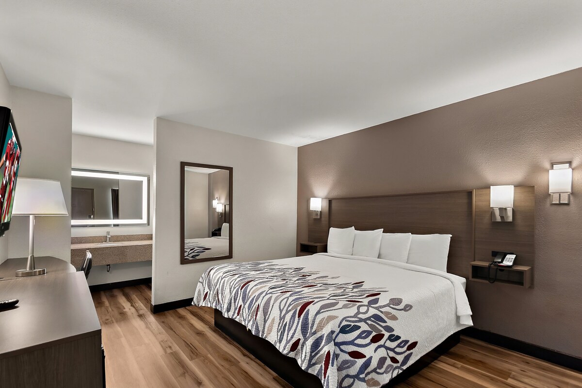 A hotel room with a large bed, bedside tables, a desk with a lamp, a mirror, and wall-mounted lights.