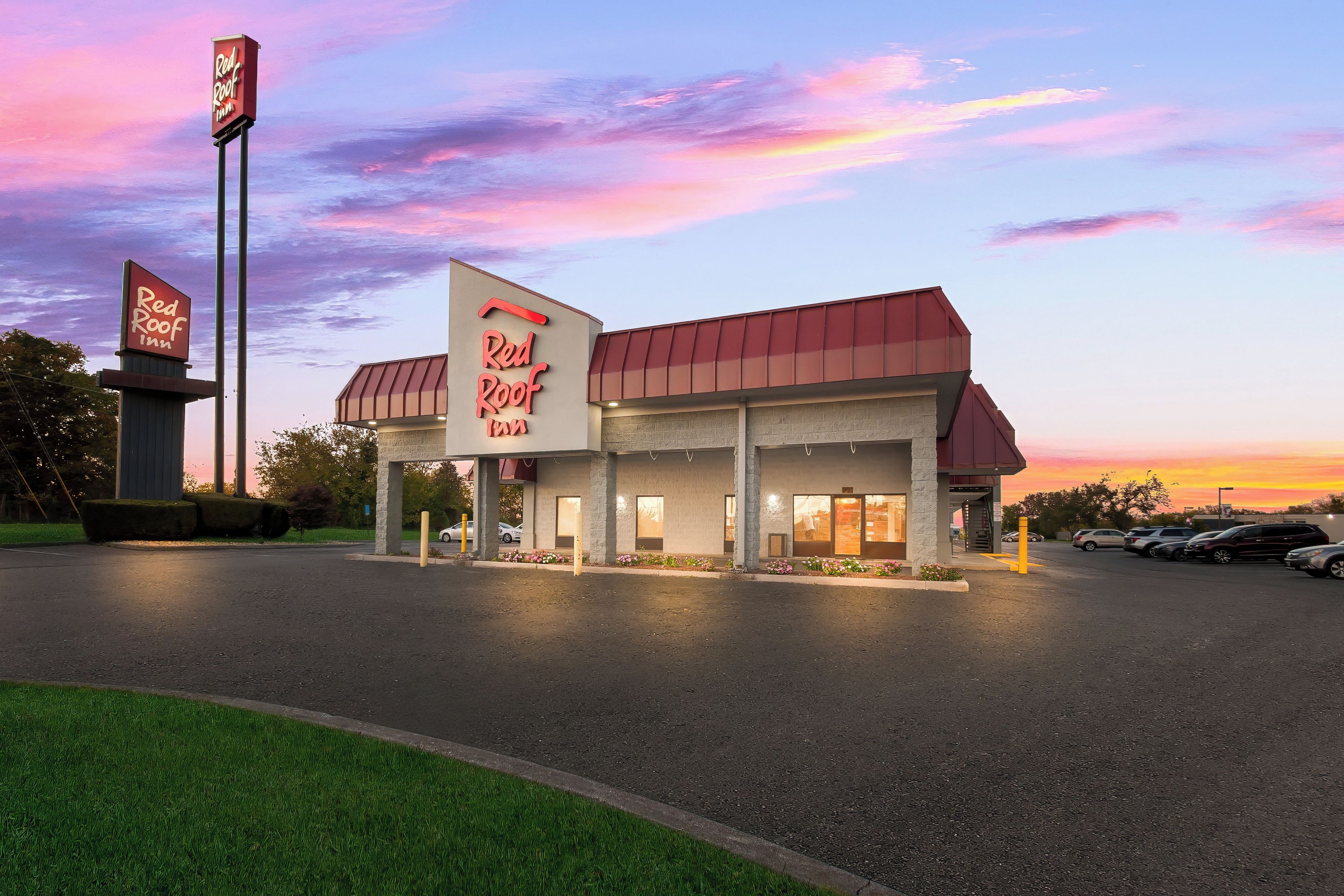 A Red Roof Inn with a large sign, a parking lot, and a sunset sky.