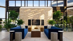 A modern outdoor lounge area with a stone fireplace, blue sofas, and potted plants. - DoubleTree by Hilton Fairfield Hotel & Suites (Fairfield)