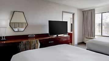 Een hotelkamer met een groot bed, een televisie op een houten dressoir, een spiegel en een raam met gordijnen.