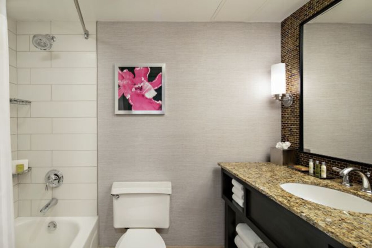 A bathroom with a white toilet, a bathtub, a granite countertop sink, and a mirror with a wooden frame.