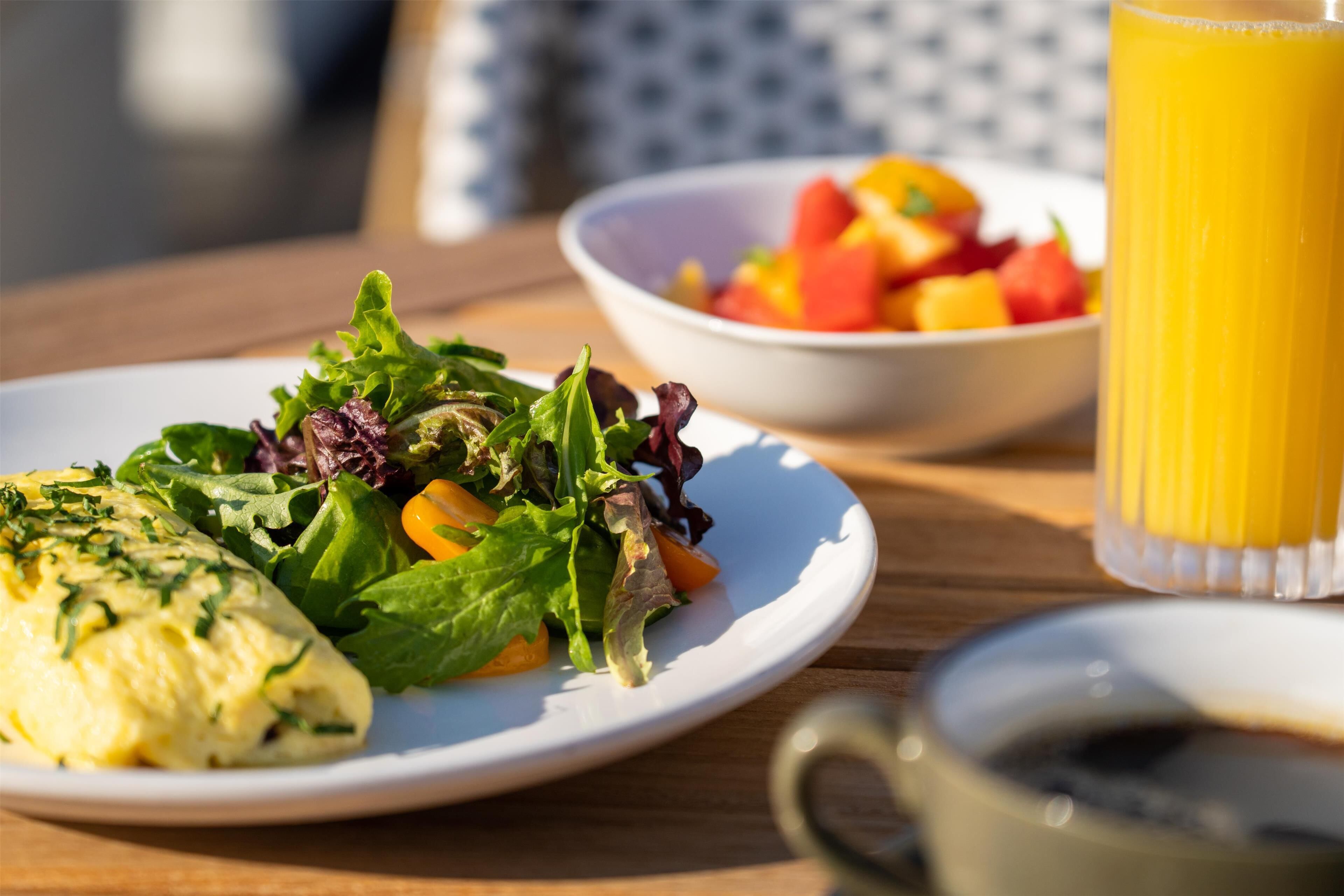 A breakfast setting with a plate of food, a bowl of fruit, and a glass of orange juice on a wooden table.