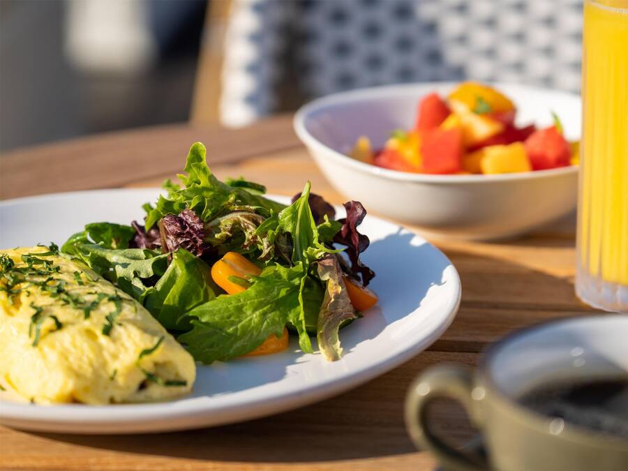 A breakfast setting with a plate of food, a bowl of fruit, and a glass of orange juice on a wooden table.
