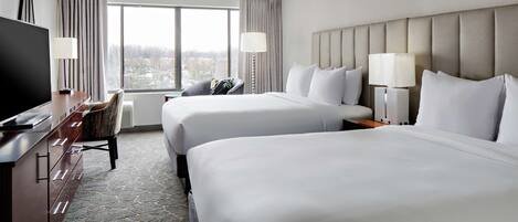 A hotel room with two beds, a desk with a TV, a chair, and a large window with curtains.
