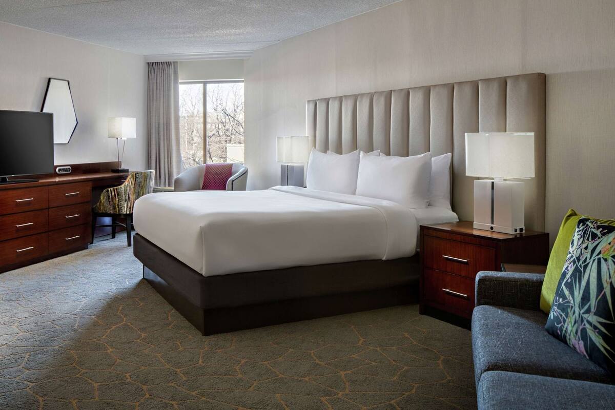 A hotel room with a large bed, a desk, a television, and a sofa.