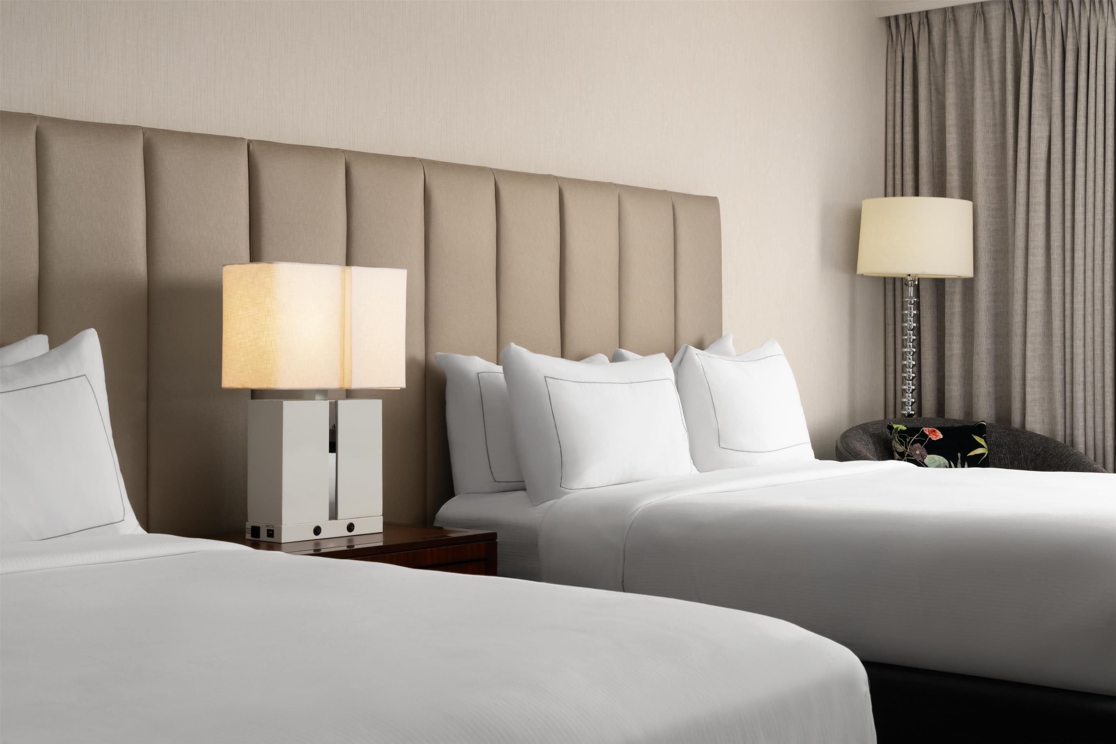 A hotel room with two beds, a headboard, a nightstand, a lamp, and a curtain.