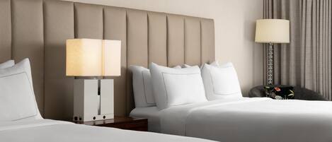 A hotel room with two beds, a headboard, a nightstand, a lamp, and a curtain.