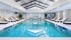 An indoor swimming pool with clear water, lounge chairs, a ceiling with a geometric pattern, and a view of the outdoors through a large window. - DoubleTree by Hilton Fairfield Hotel & Suites (Fairfield)
