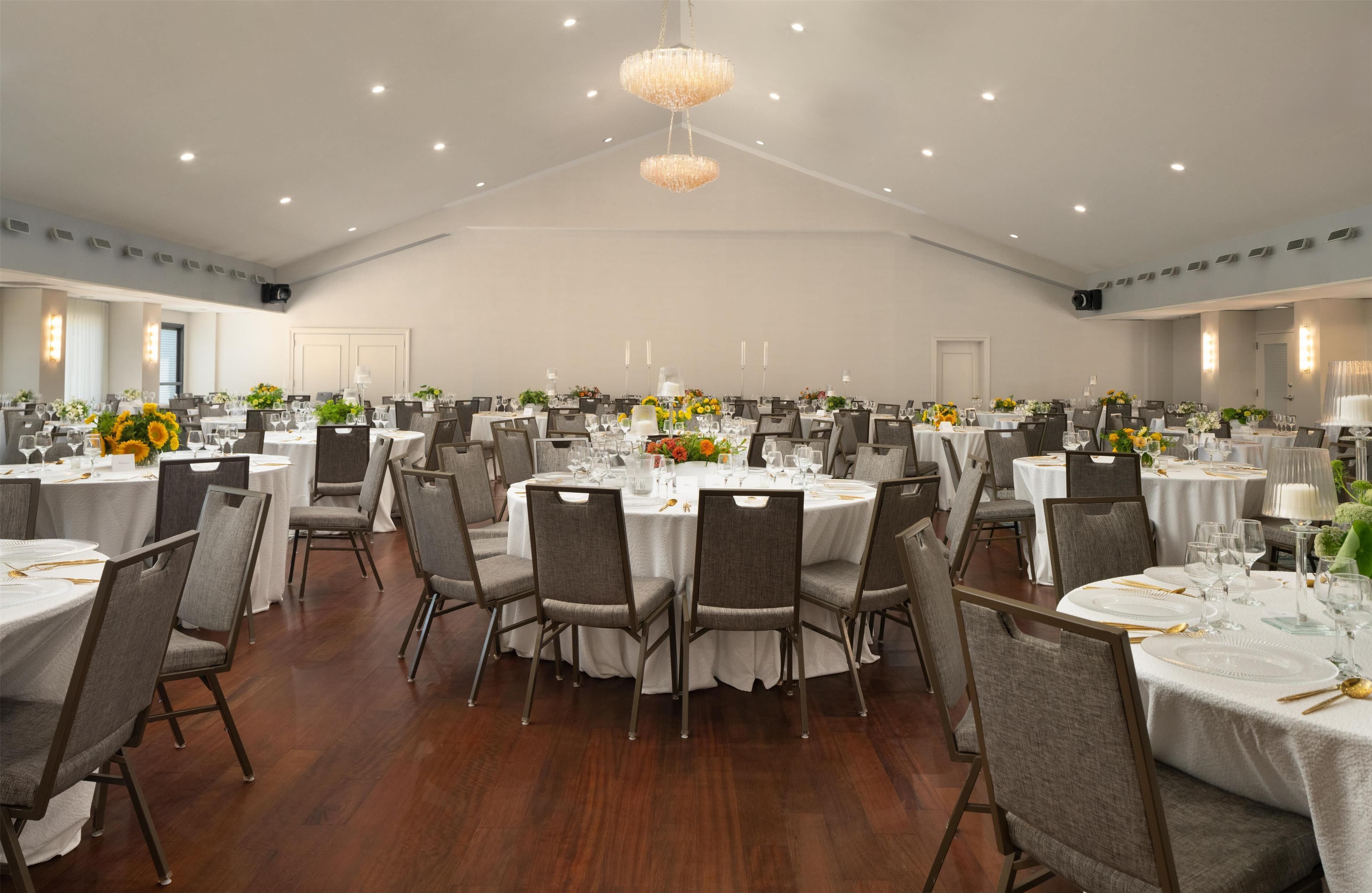 A large banquet hall with round tables, grey chairs, and white tablecloths.