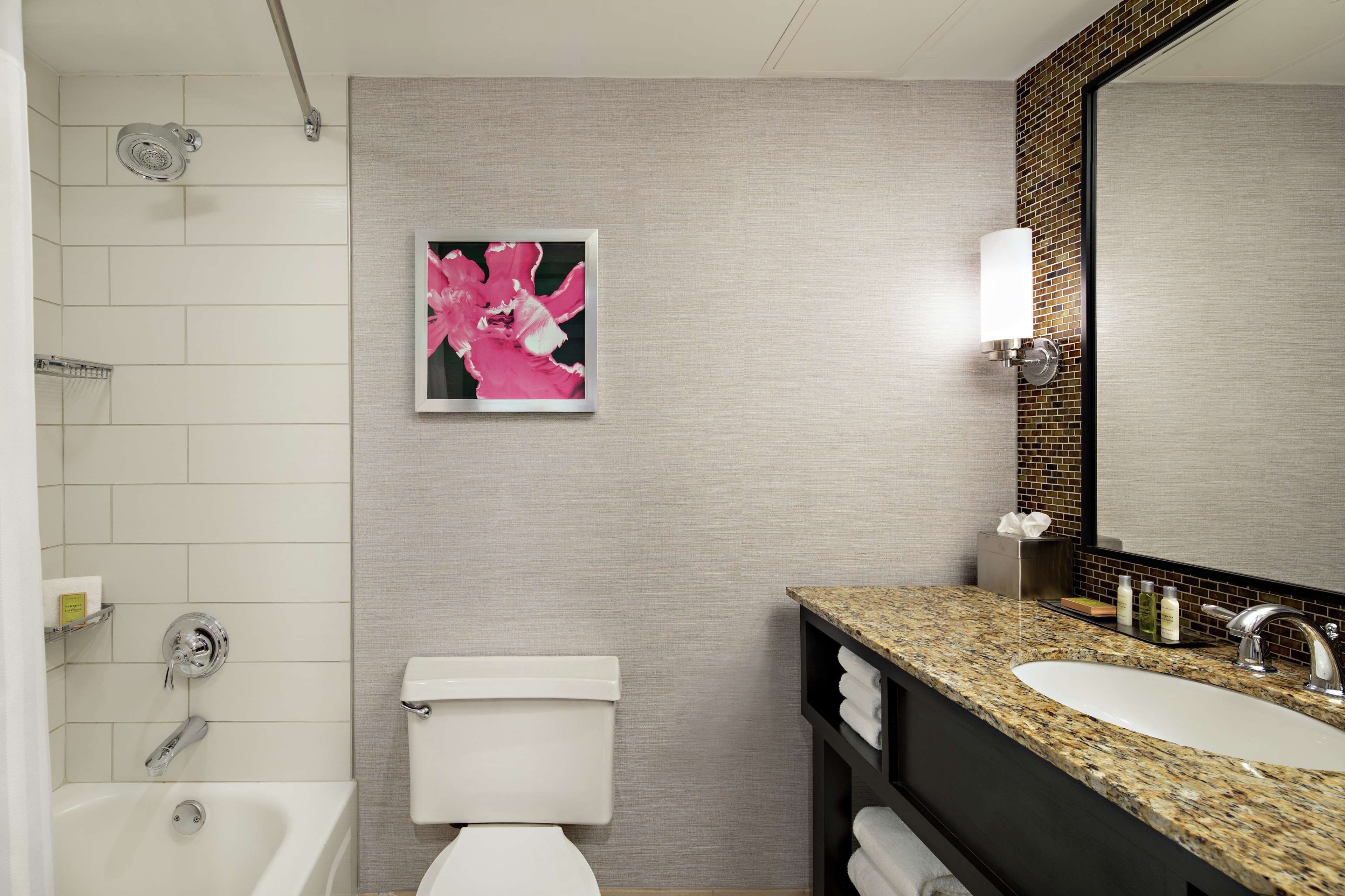 A modern bathroom with a white bathtub, a toilet, a granite countertop sink, and a large mirror.