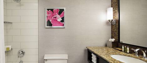 A modern bathroom with a white bathtub, a toilet, a granite countertop sink, and a large mirror.