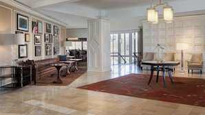 A spacious lobby with a high ceiling, a large red rug, a brown leather bench, a round table with a lamp, and framed pictures on the walls. - Sheraton Westport Chalet Hotel St. Louis (Maryland Heights)