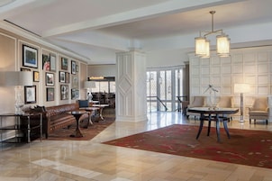 A spacious lobby with a high ceiling, a large red rug, a brown leather bench, a round table with a lamp, and framed pictures on the walls.