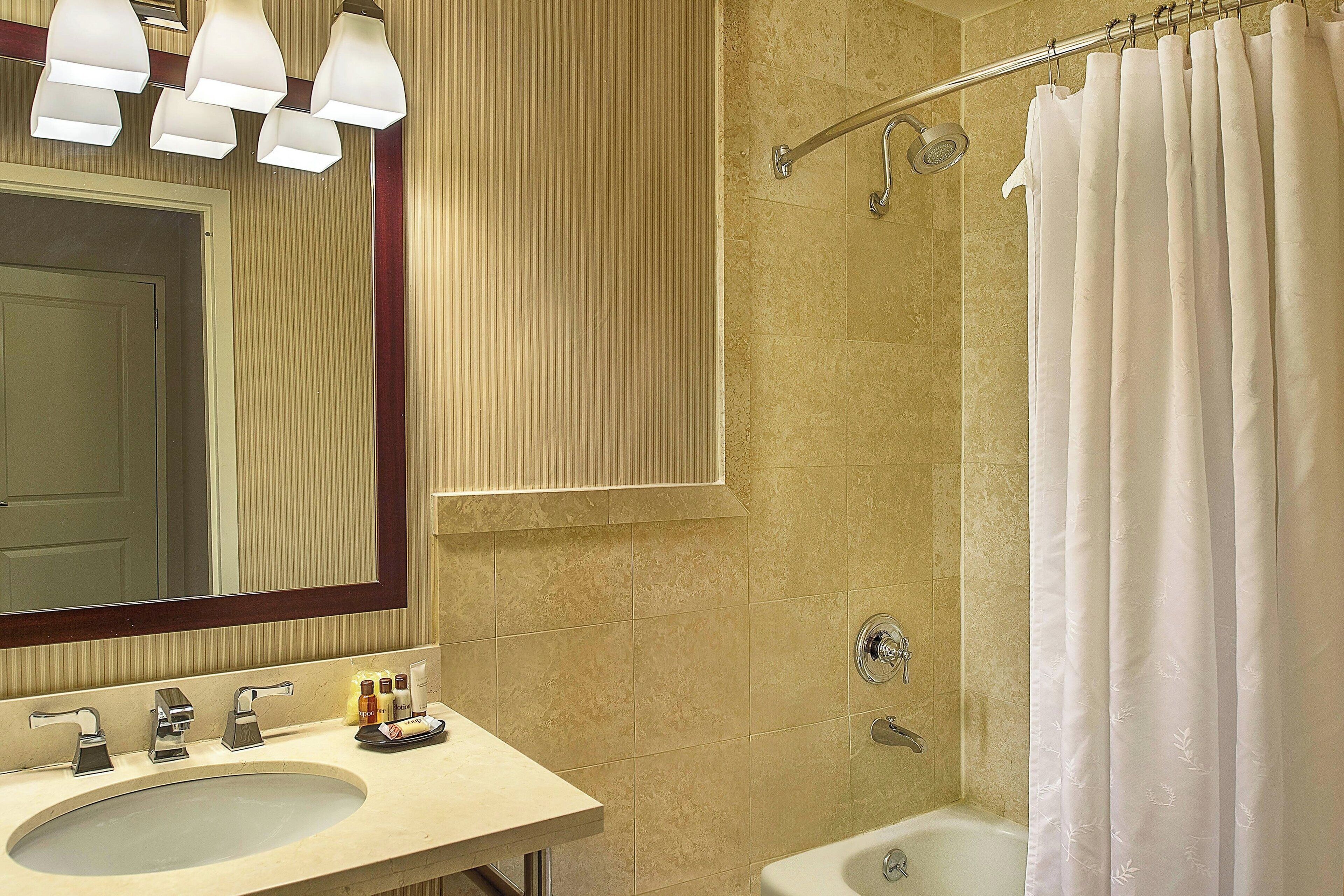 A bathroom with a sink, mirror, shower, and towel rack.