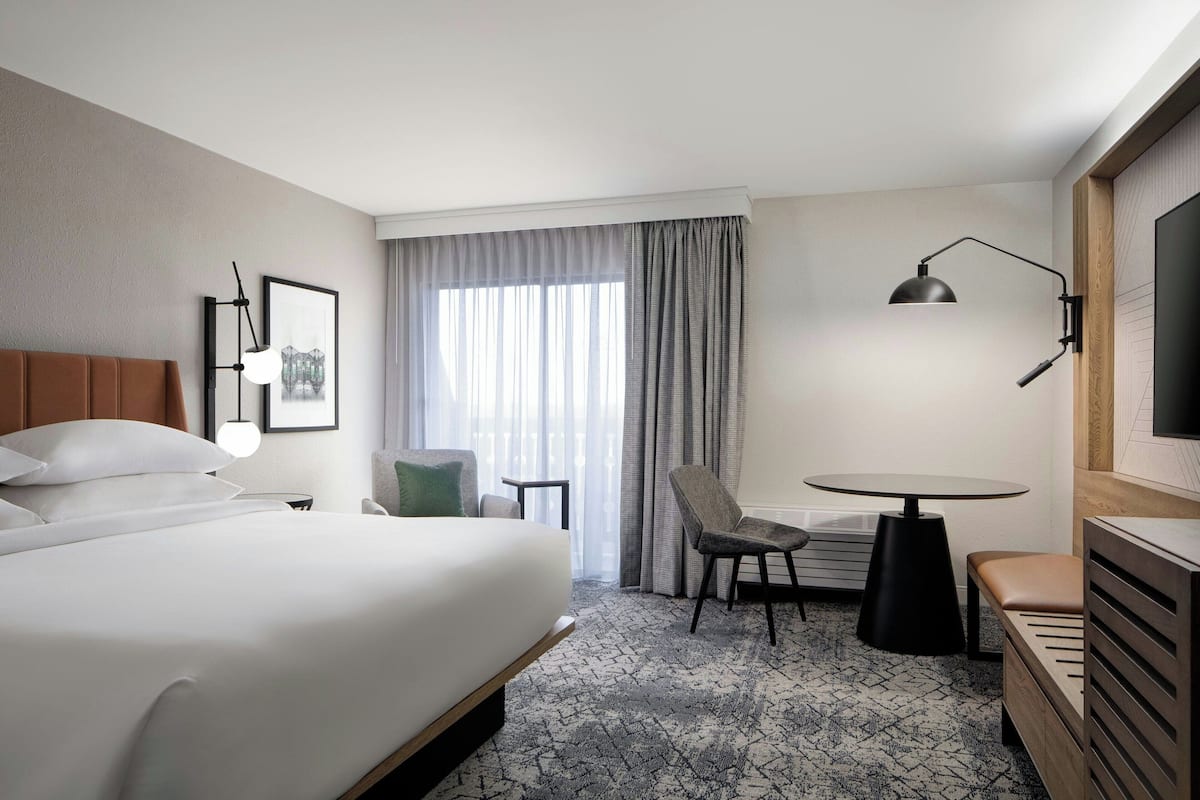 A hotel room with a large bed, a desk, a chair, a TV, and a window with curtains.