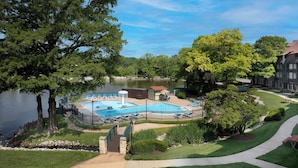 A swimming pool with a water slide, surrounded by a fence, near a lake with trees and buildings in the background. - Sheraton Westport Chalet Hotel St. Louis (Maryland Heights)