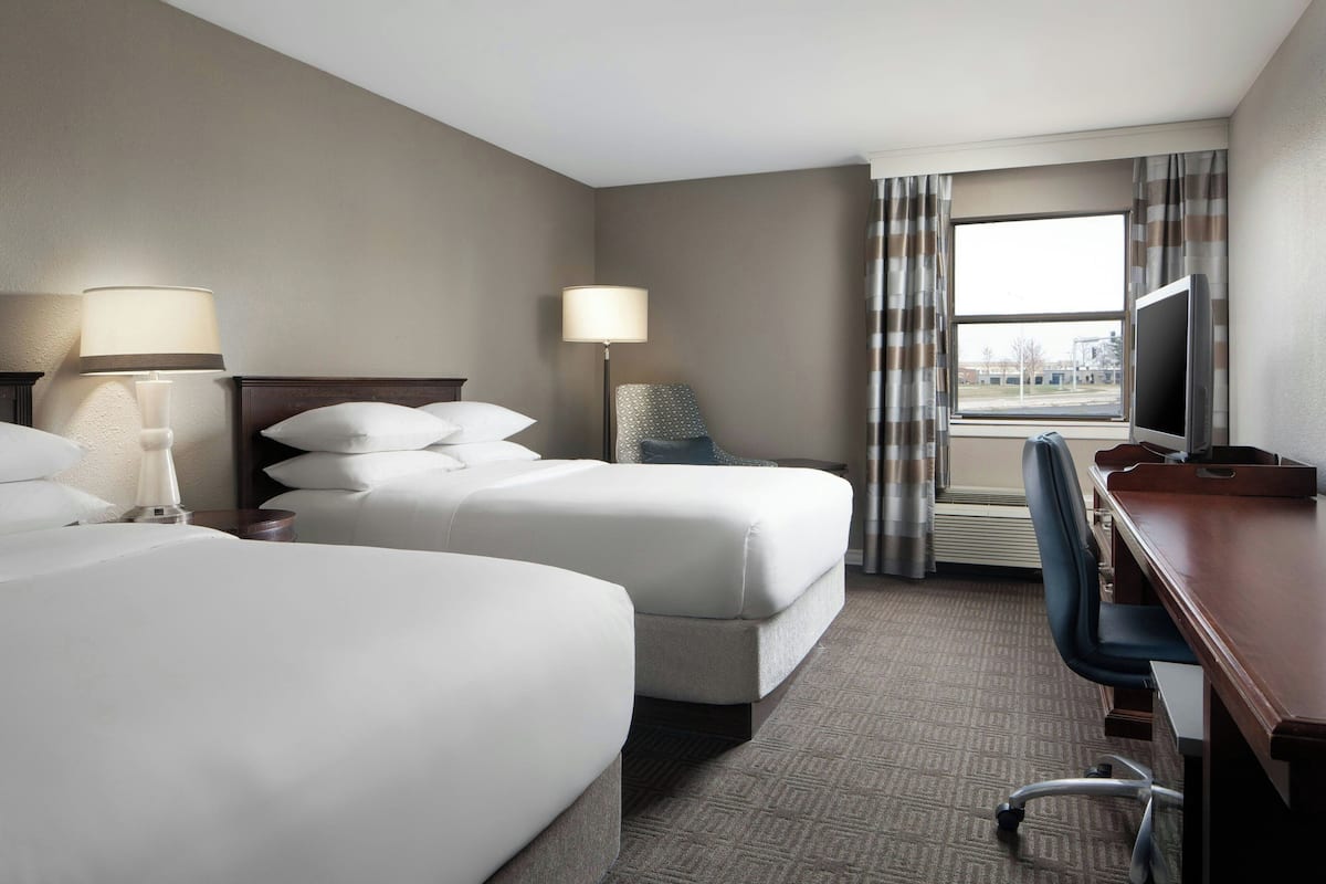 A hotel room with two beds, a desk, a chair, a TV, and a window with curtains.