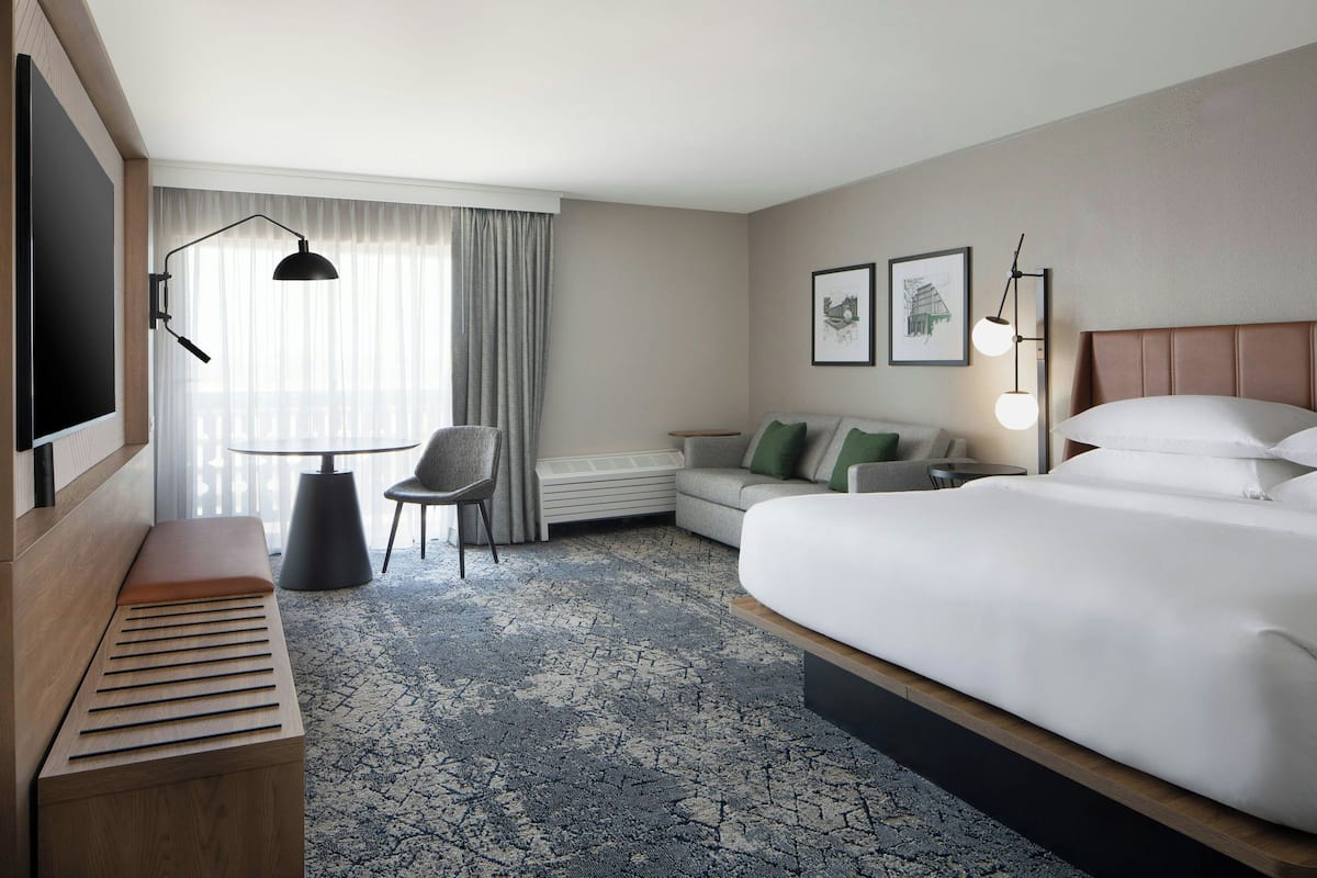 A hotel room with a bed, a desk, a chair, a small table, and a TV.