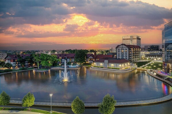 Vista de un lago con un hotel, una fuente, árboles y edificios modernos.
