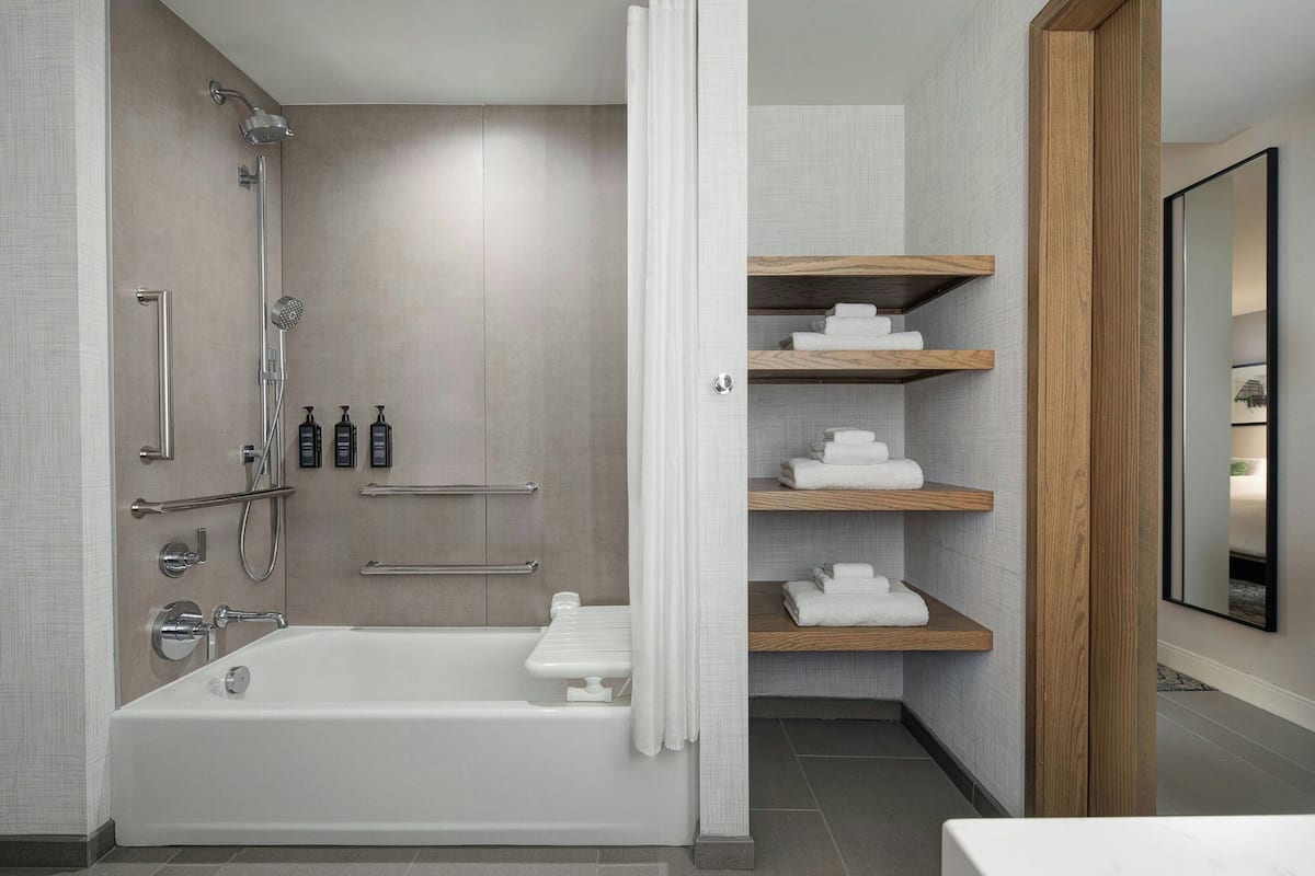 A modern bathroom with a bathtub, shower, and wooden shelves with towels.