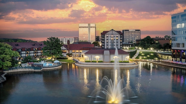 A waterfront hotel with a central fountain, a pool, and a view of the city skyline at sunset. - Sheraton Westport Chalet Hotel St. Louis (Maryland Heights)